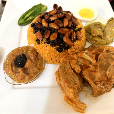 Un exemple de couscous tunisien : une salade mechaoia composée de poivrons et tomates rôties garnies de thon, du couscous garni d’amandes et de raisins secs, de la viande d’agneau et un œuf cuit dur. Source : Asma Mokhtar. Photo d'une assiette de couscous tunisien.