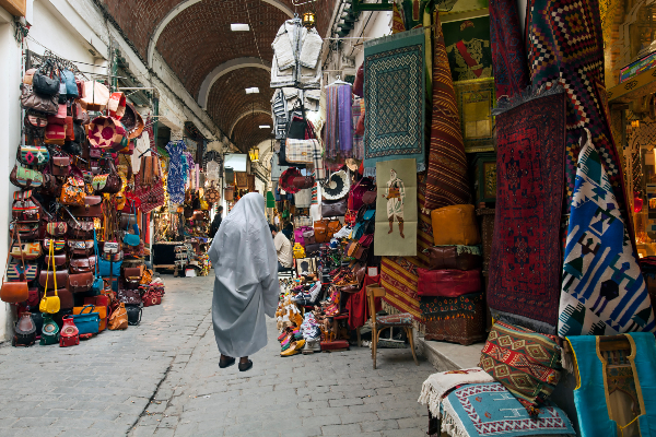 Le souk de la médina de Tunis ou, autrement dit, le marché de la partie ancienne de la ville. On y trouve toutes sortes de choses, de la nourriture aux vêtements, en passant par les produits artisanaux. Source : Getty Images. Une femme marche dans une allée de la médina.