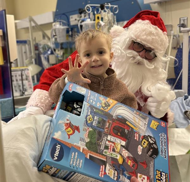 Un jeune patient assis sur les genoux du Père Noël reçoit un cadeau.